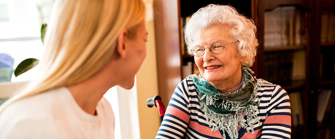 A caregiver and an elderly woman having a conversation in a sunny room